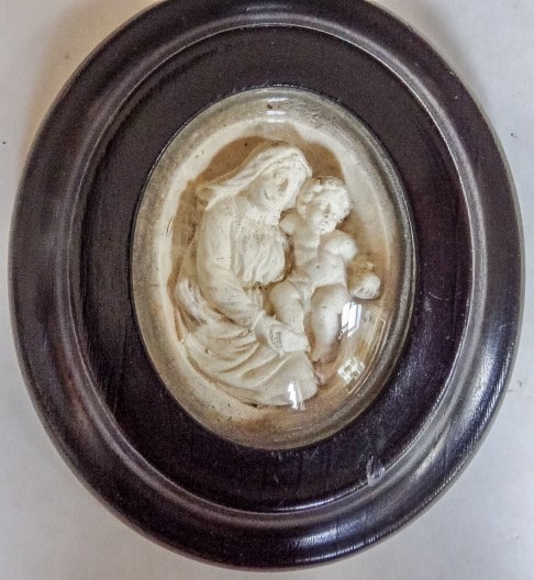 Ovale houten lijst achter glas met een gipsen reliëf van Maria met Kind.