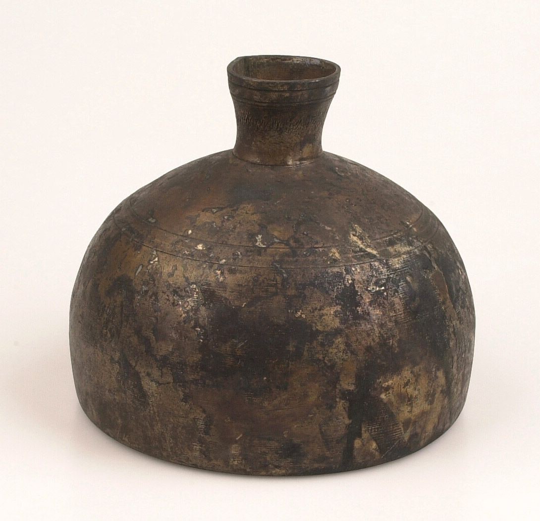 Bolvormige tinnen fles met korte, smalle hals, donker en vlekkerig verweerd, tegen een lichte achtergrond.