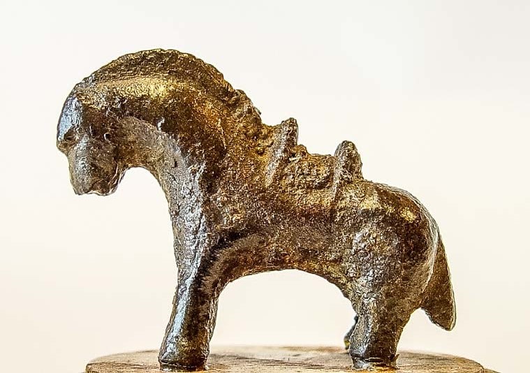Bronzen paardje op een sokkeltje, van opzij gefotografeerd tegen een lichte achtergrond.