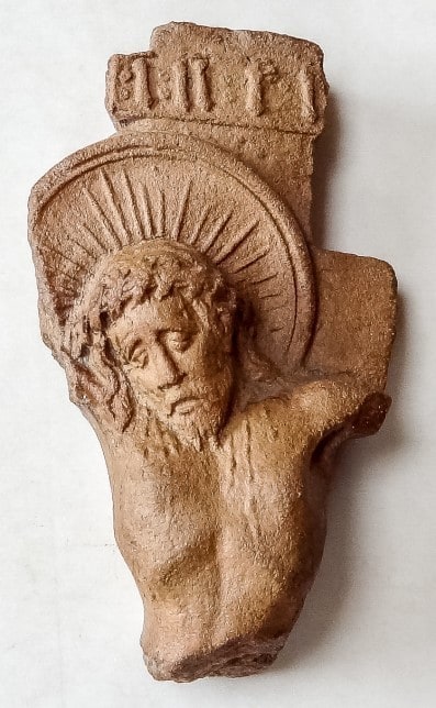 Roodbakkend fragment met het hoofd en bovenlijf van de gekruisigde Christus onder een stralenkrans.