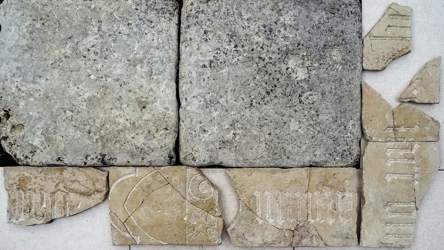 Reconstructie van de stroken natuursteen met tekst en wapenschild, gelegd tussen twee kalkstenen vloertegels.