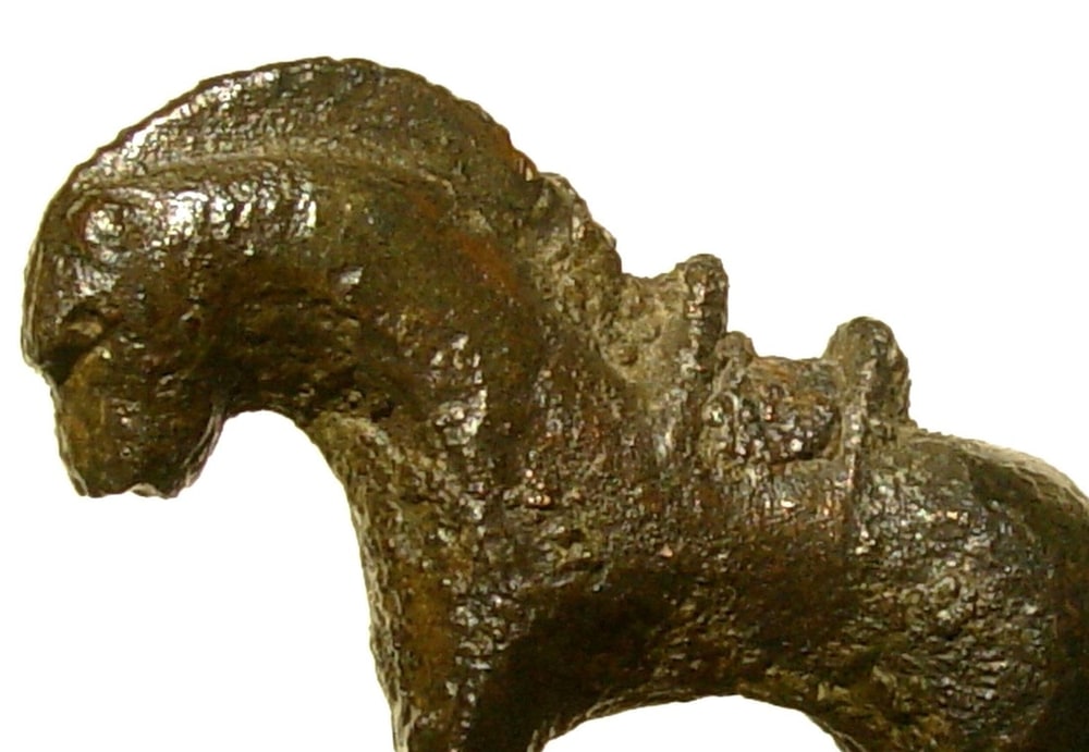 Detail van de naar links gerichte kop, de manen en de ruwe, bruingroene huid van het bronzen paardje.