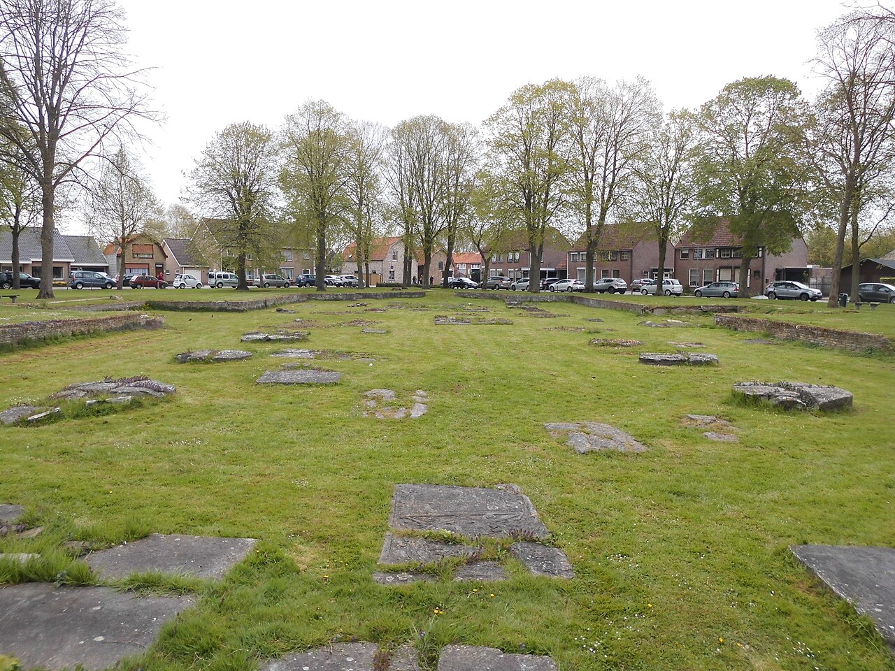 Grafzerken in het gras en lage kerkfunderingen op het Sint-Janskerkhof in Sluis.