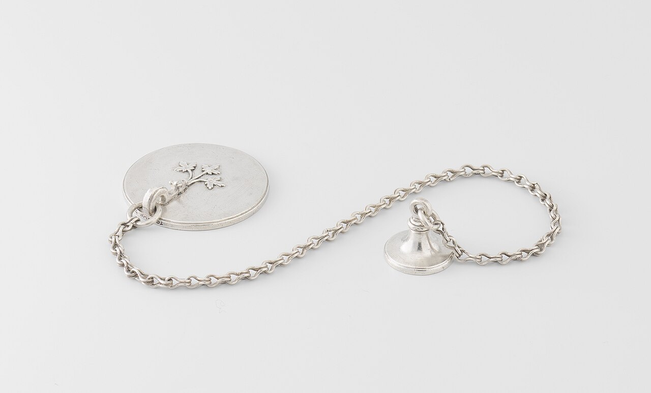 Een zilveren zegelstempel en kleinere contrazegelstempel, verbonden door een ketting.